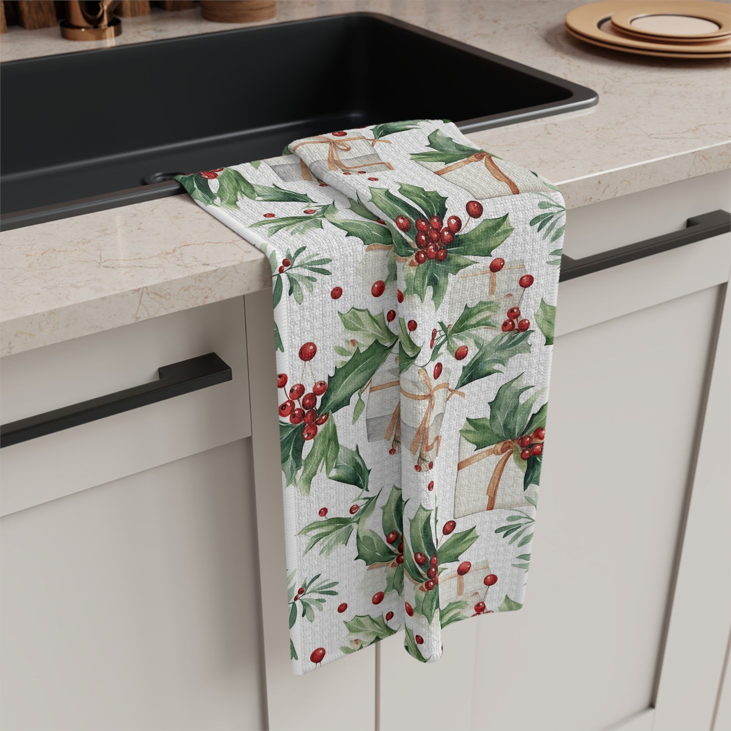 White microfiber tea towel with watercolor holly, red berries, and gift pattern draped over a kitchen sink.