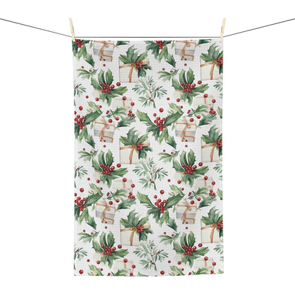 Microfiber tea towel with watercolor holly, red berries, and wrapped gifts, hanging on a clothesline.