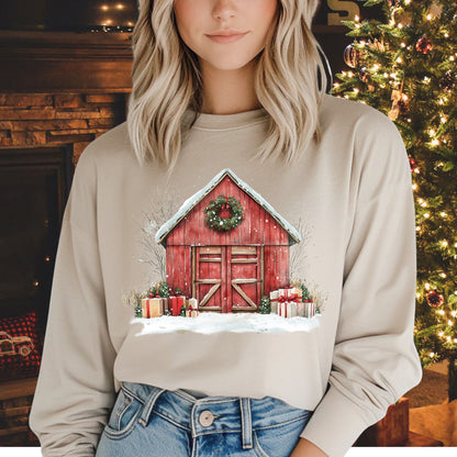 Woman in a beige long sleeve tee with a watercolor red barn, snow, gifts, and wreath design.