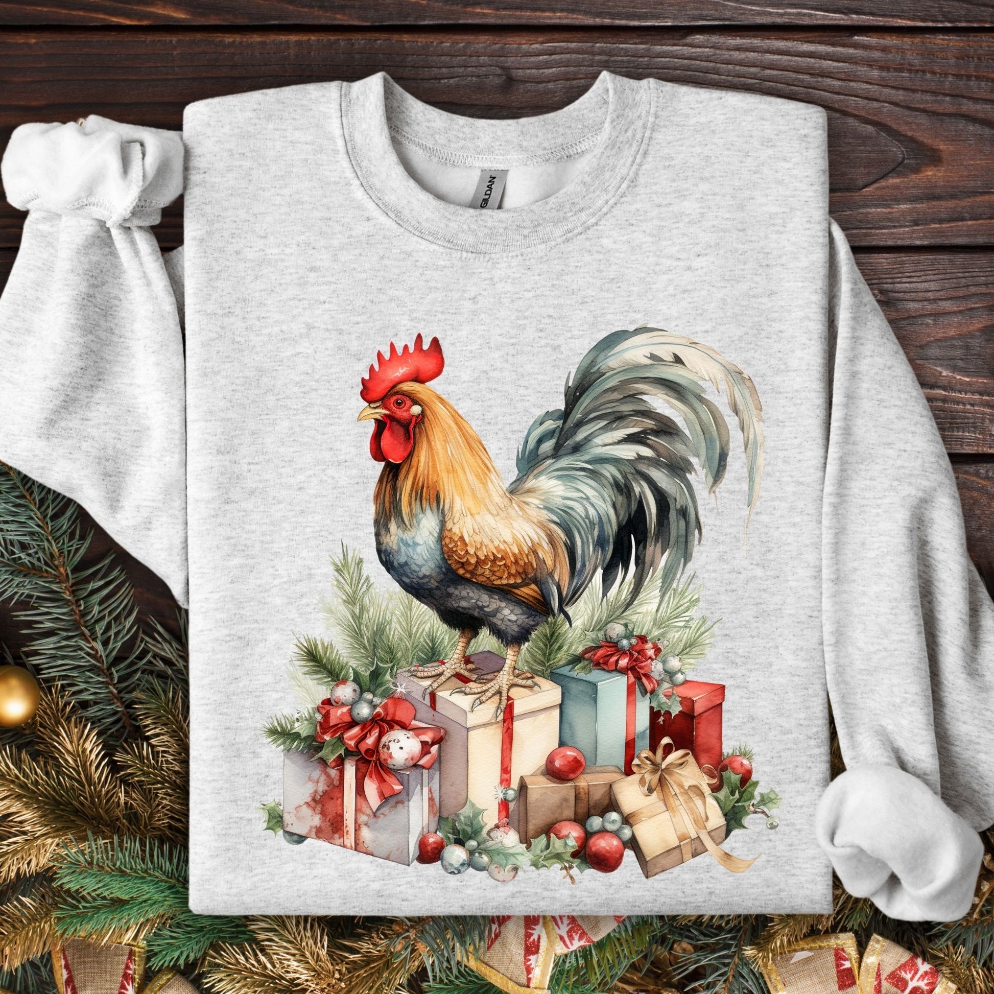 Ash Gildan sweatshirt with a colorful watercolor rooster standing on Christmas gifts and pine branches.