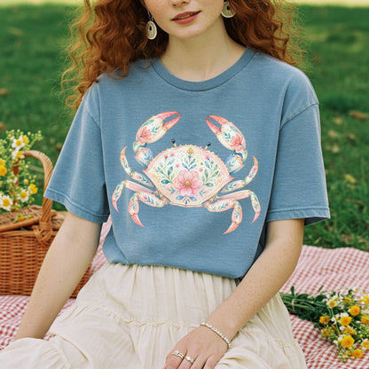 Relaxed-fit, garment-dyed blue t-shirt with a watercolor floral crab design, worn by a person on a picnic blanket.