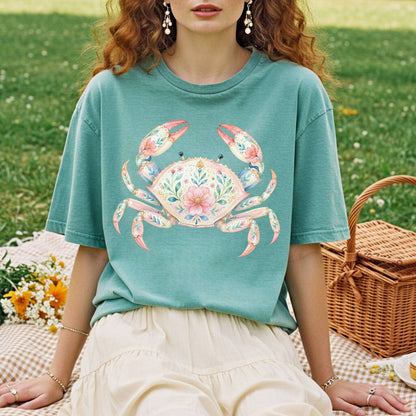 Garment-dyed teal t-shirt with a watercolor floral crab design, worn by a person on a picnic blanket.