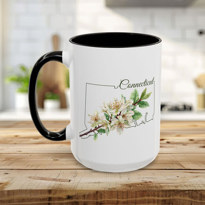 White ceramic mug with black handle and interior, featuring a watercolor Mountain Laurel bloom over a Connecticut outline.