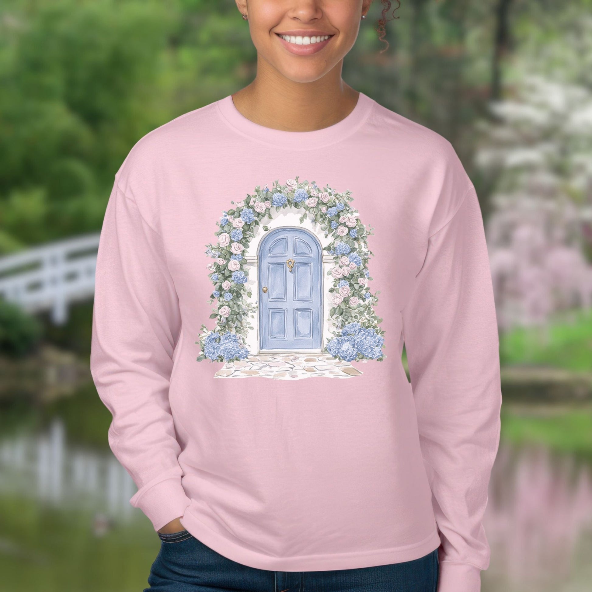 Pink long-sleeve tee with a watercolor blue cottage doorway and climbing pink and blue hydrangeas.