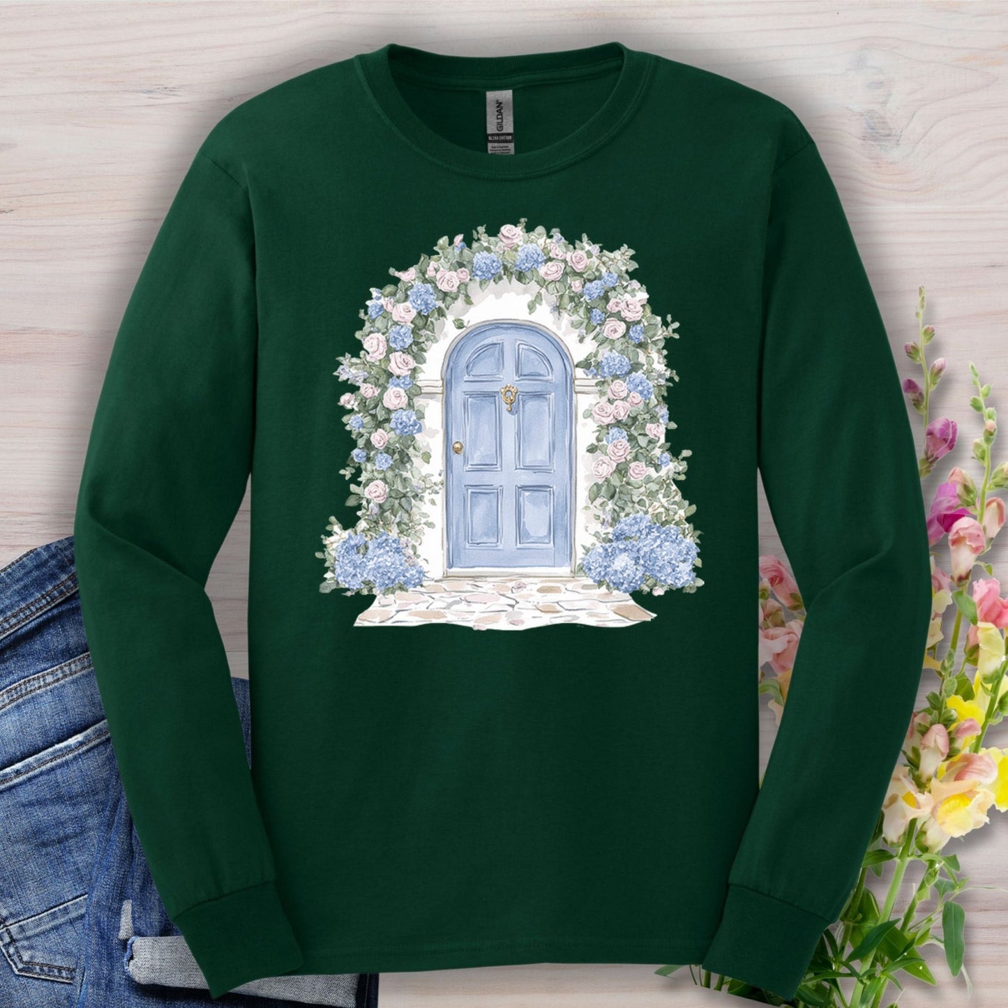 Forest Green long-sleeve tee with a watercolor blue cottage door, pink roses, and blue hydrangeas.