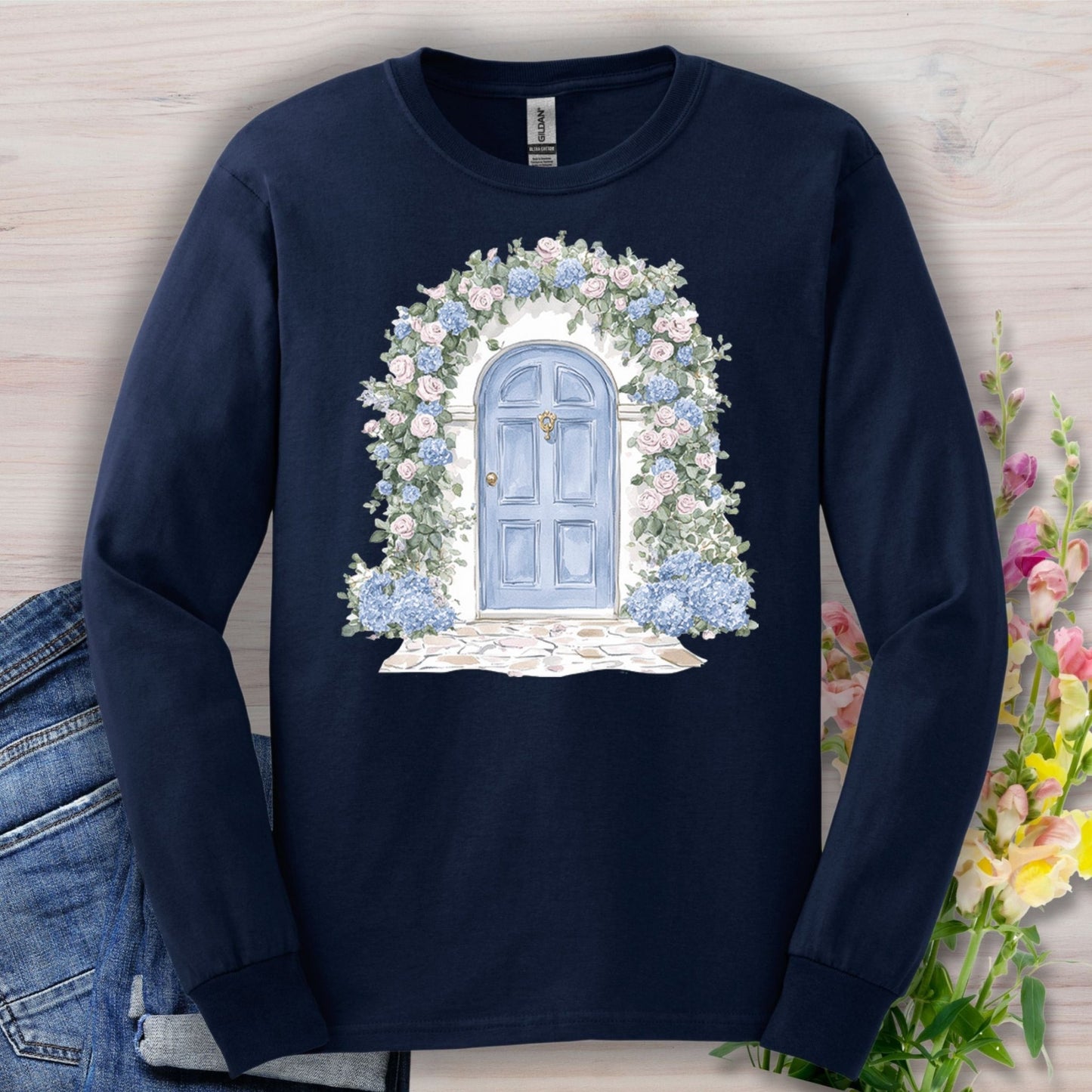 Navy long-sleeve tee with a hand-painted blue cottage doorway, climbing roses, and hydrangeas.
