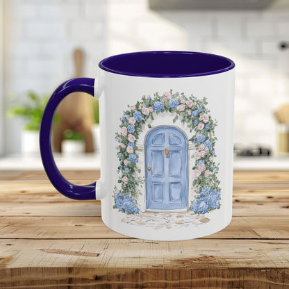 White ceramic mug with a blue cottage door, pink roses, and blue hydrangeas, featuring a purple handle and interior.