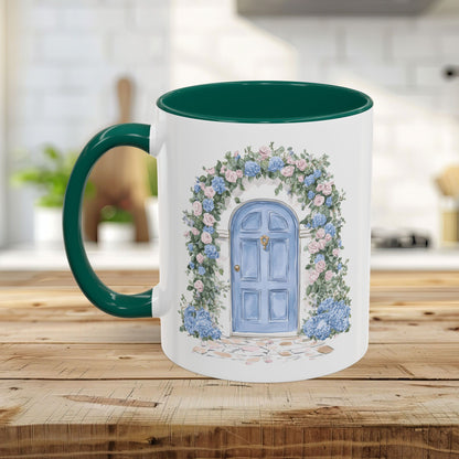 White ceramic mug with green handle and interior, featuring a watercolor blue cottage door framed by pink roses and blue hydrangeas.