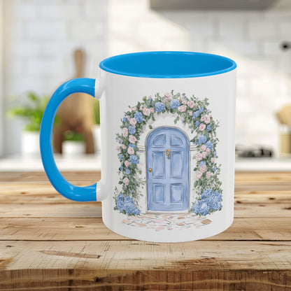 White ceramic mug with blue interior and handle, featuring a watercolor cottage doorway with pink roses and blue hydrangeas.