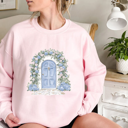Pink sweatshirt with a watercolor cottage doorway, blue door, and pink and blue hydrangeas.