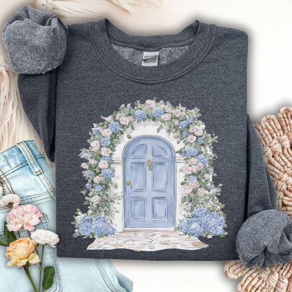 Dark Heather sweatshirt with a watercolor cottage doorway framed by pink roses and blue hydrangeas.