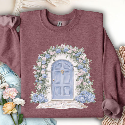 Heather Sport Dark Maroon sweatshirt with a watercolor cottage doorway framed by blue hydrangeas and pink roses.