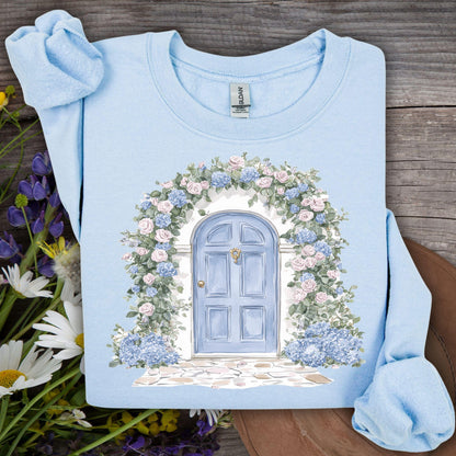 Light blue sweatshirt with watercolor cottage doorway, pink roses, blue hydrangeas, and eucalyptus.