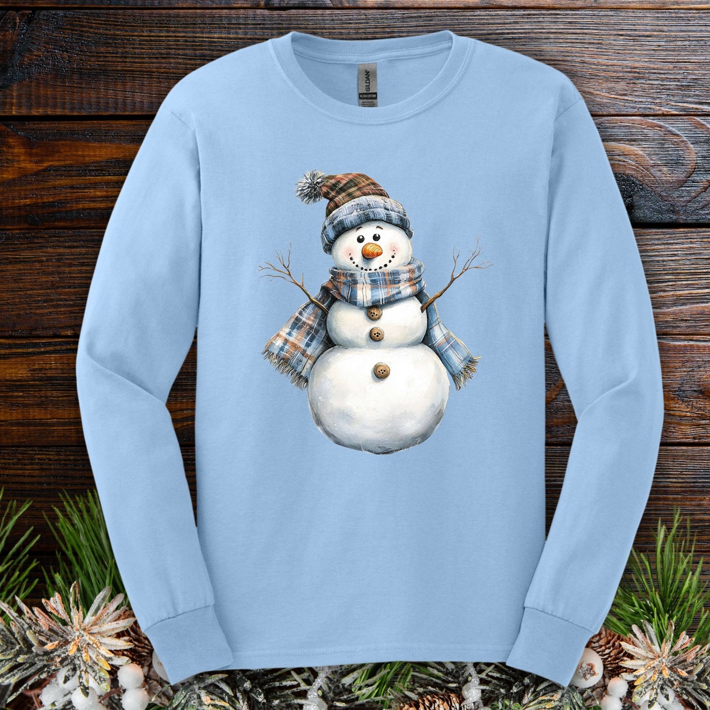 Light blue long sleeve tee with a snowman wearing a blue and tan plaid hat and scarf.