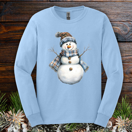 Light blue long sleeve tee with a snowman wearing a blue and tan plaid hat and scarf.