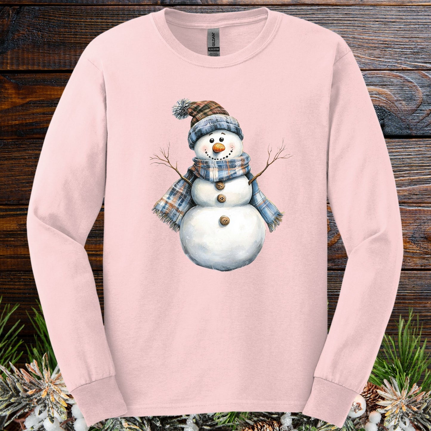 Light pink long sleeve tee with a snowman wearing a blue and tan plaid scarf and hat.