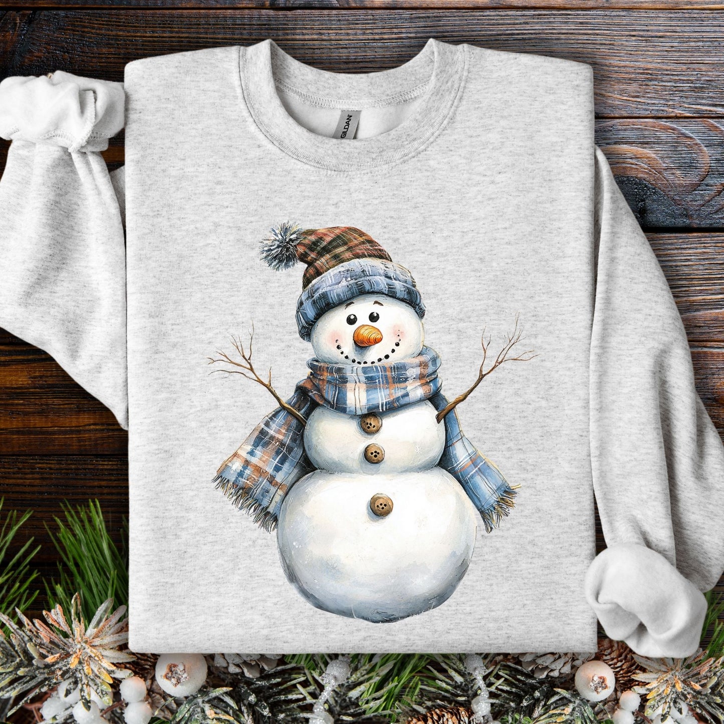 Ash gray heavy blend sweatshirt with a watercolor snowman in a blue and tan plaid scarf and hat.