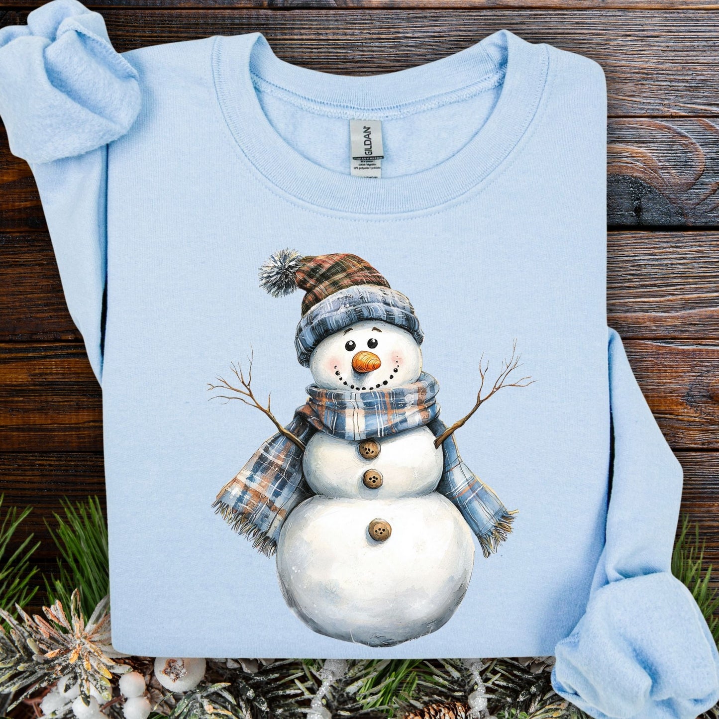 Light blue snowman sweatshirt with watercolor art of a snowman in a blue and tan plaid scarf and hat.
