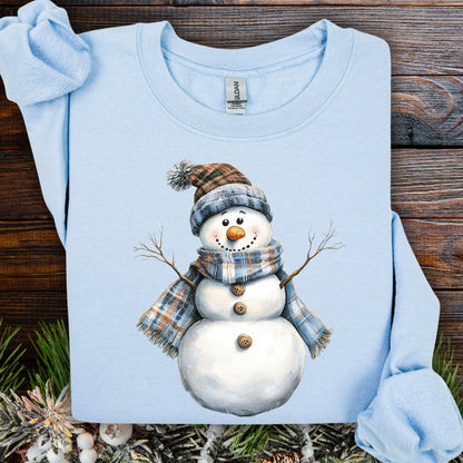 Light blue snowman sweatshirt with watercolor art of a snowman in a blue and tan plaid scarf and hat.