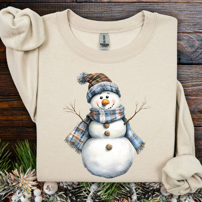 Sand heavy blend sweatshirt with a watercolor snowman in a blue and tan plaid scarf and hat.