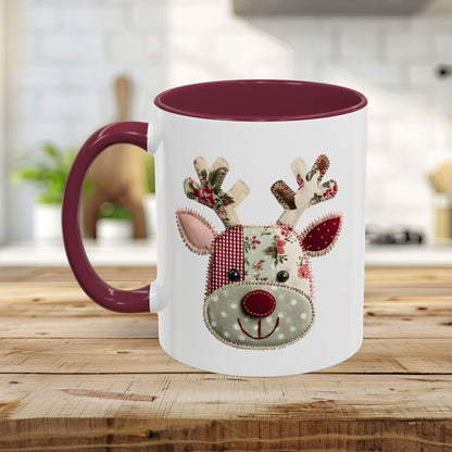 White ceramic mug with a patchwork Rudolph design, burgundy interior, and handle on a wooden table.