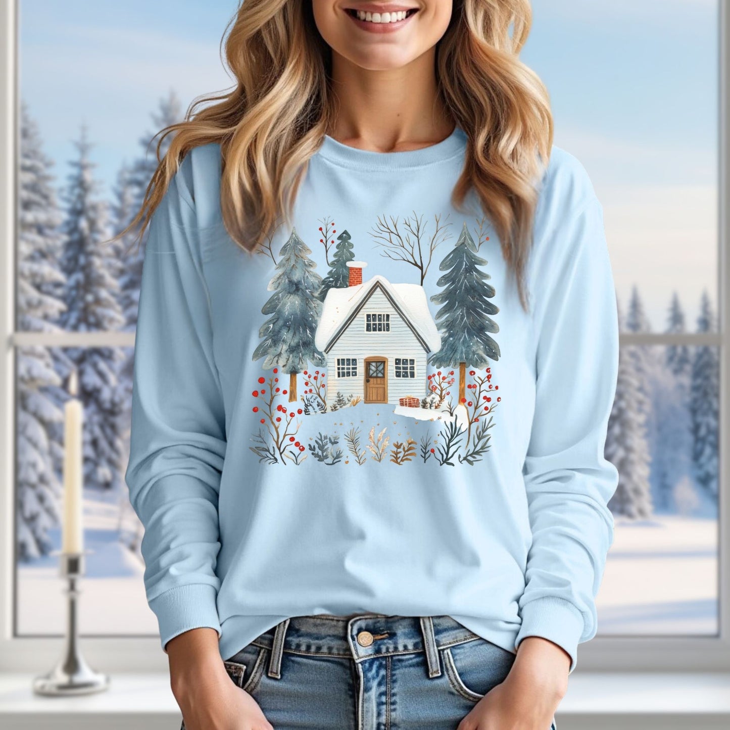 Woman in a light blue long-sleeve tee with a hand-drawn winter cabin and pine trees design.