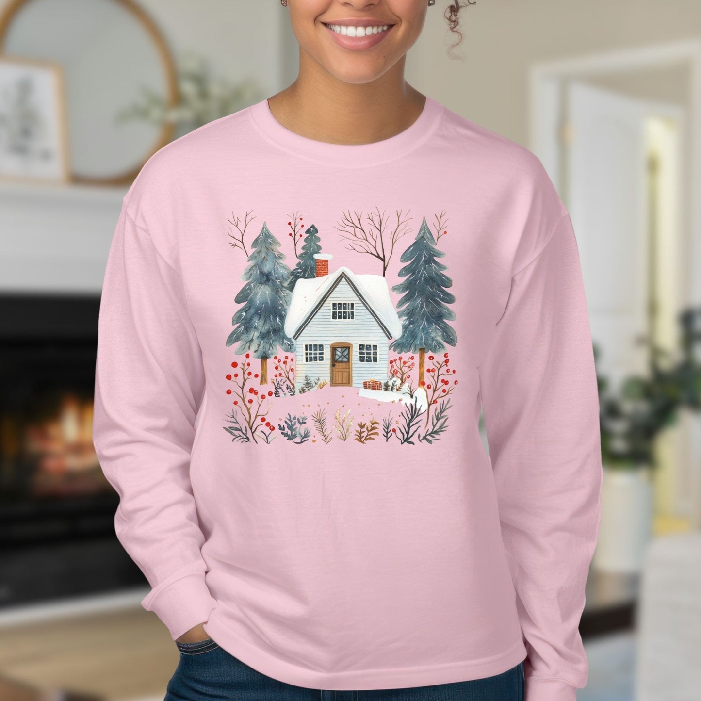 Pink long sleeve tee with a hand-drawn winter cabin and pine tree design, worn by a smiling person.