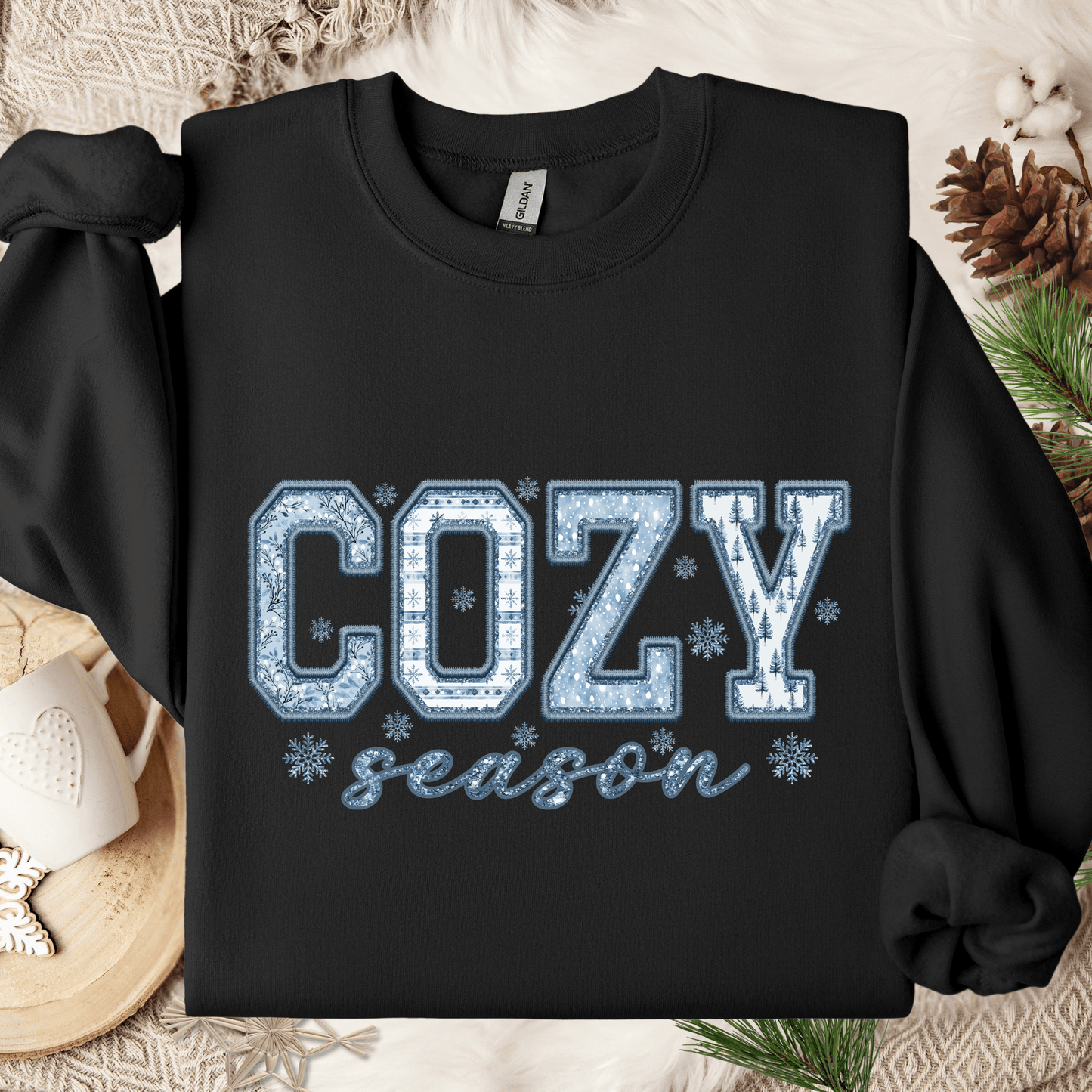 Black heavy blend sweatshirt with "COZY season" in blue and white faux patchwork and snowflakes.