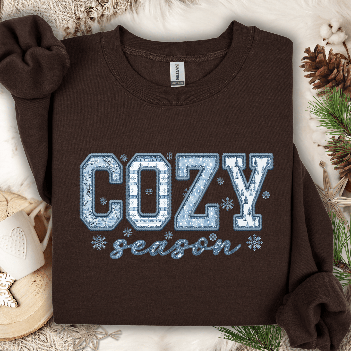 Dark chocolate Gildan heavy blend sweatshirt with "COZY season" faux patchwork print in blue and white.