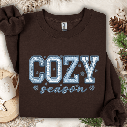 Dark chocolate Gildan heavy blend sweatshirt with "COZY season" faux patchwork print in blue and white.