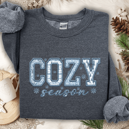 Dark heather gray sweatshirt with "COZY season" in blue and white faux patchwork print, surrounded by winter decor.
