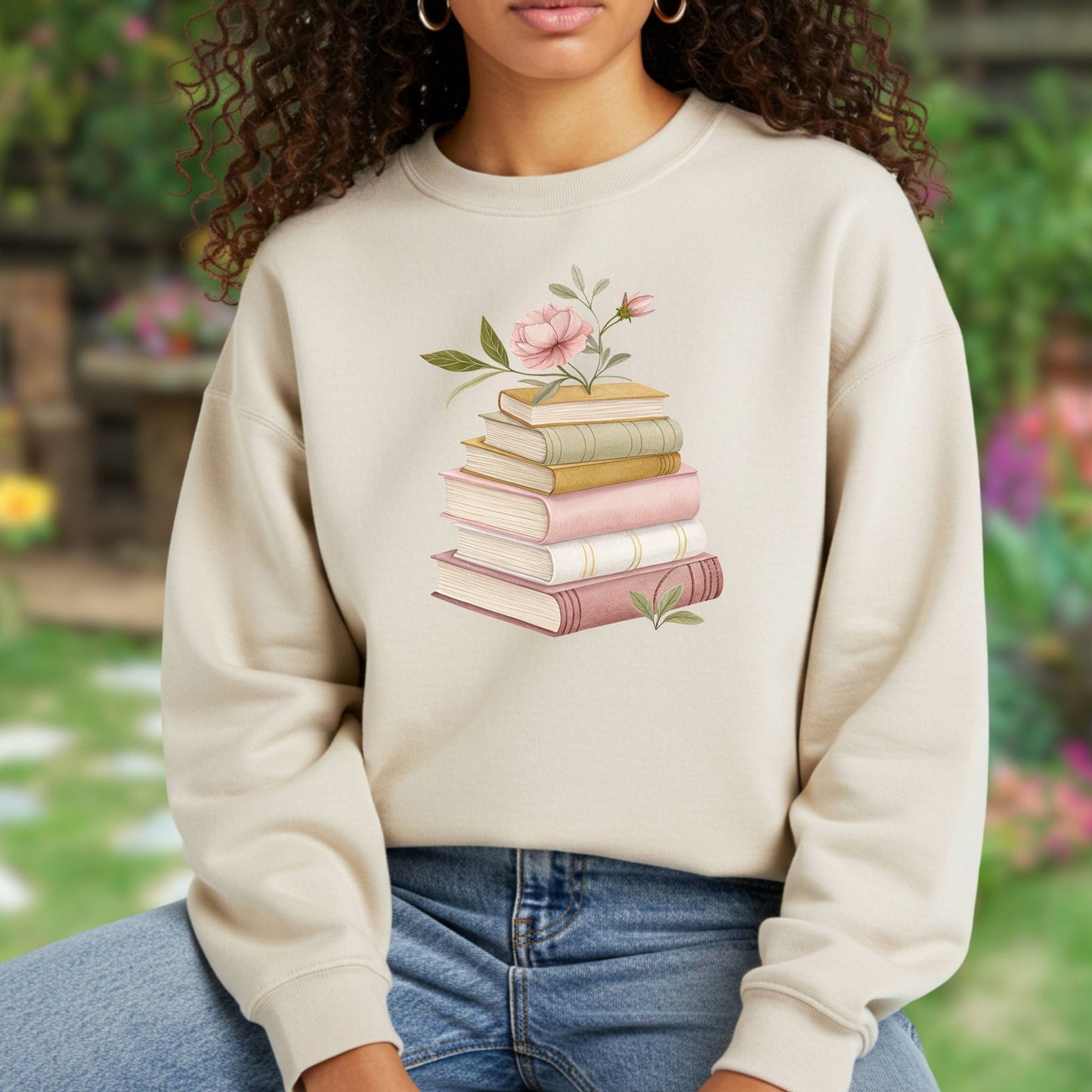 Woman in beige sweatshirt with botanical art illustration of stacked books and pink flowers.