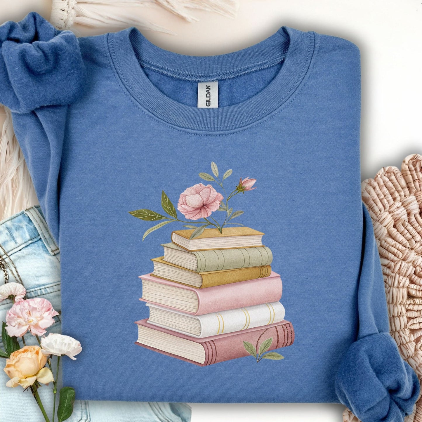 Indigo blue sweatshirt with a botanical illustration of stacked books and pink flowers.
