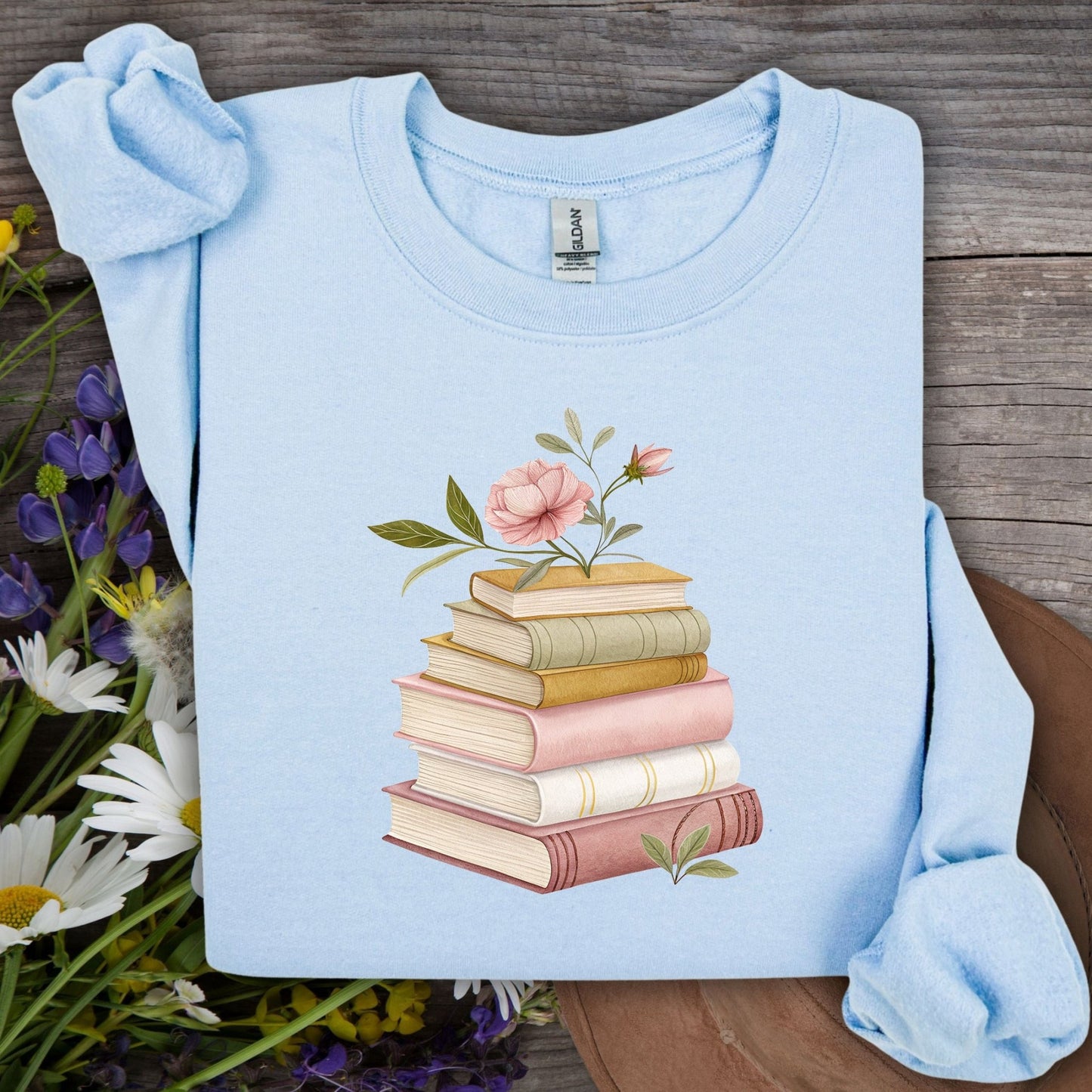 Light blue sweatshirt with a botanical illustration of stacked books and pink flowers.