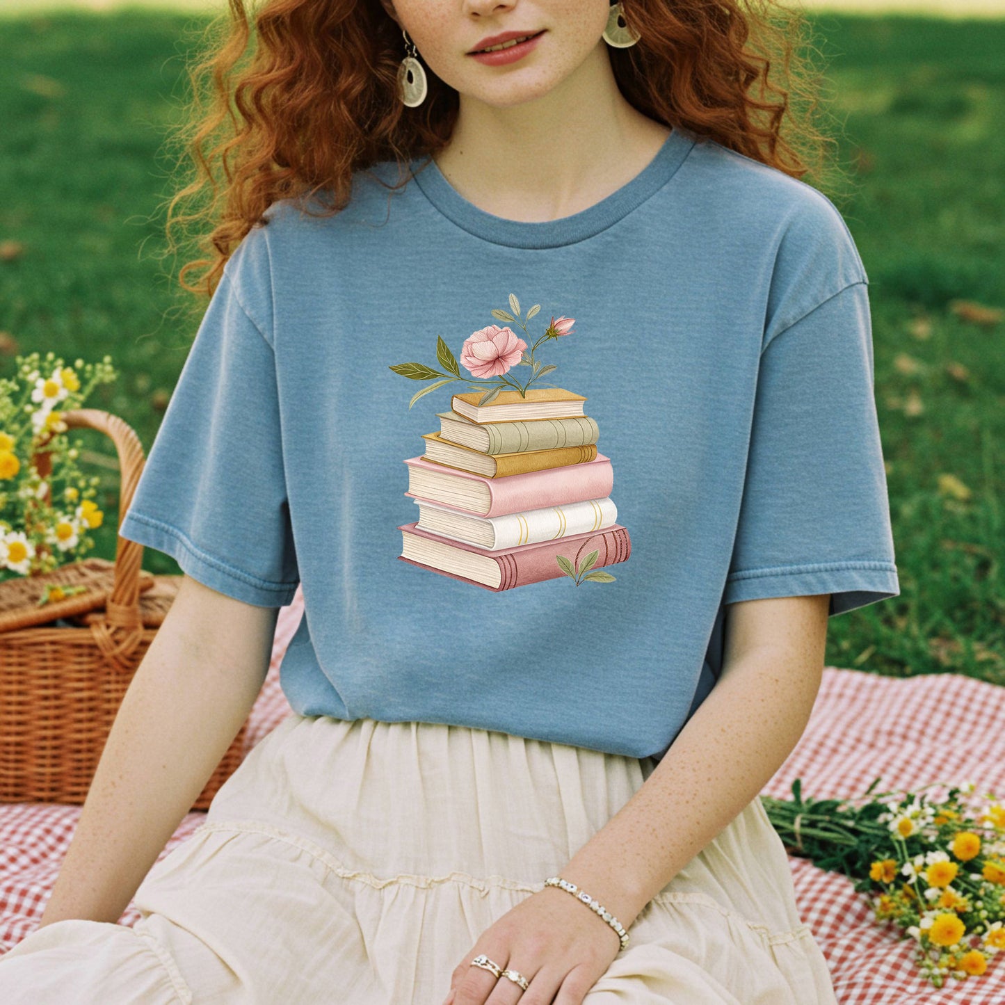 Garment-dyed blue t-shirt with a watercolor stack of books and a pink floral illustration.