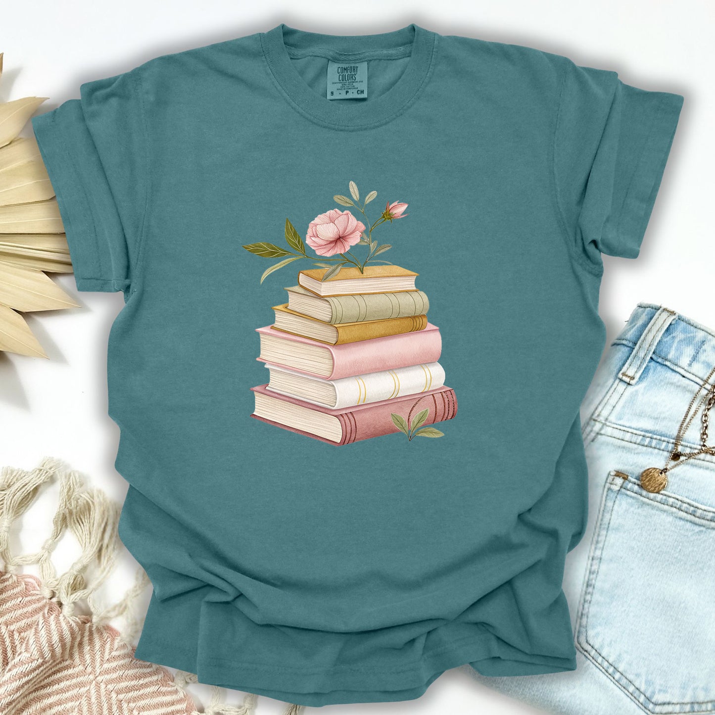 Blue Spruce garment-dyed cotton t-shirt with a watercolor stack of books and pink floral design.