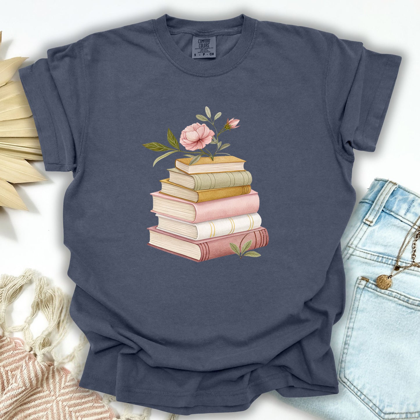 Denim S garment-dyed t-shirt with a watercolor stack of books and pink floral illustration.