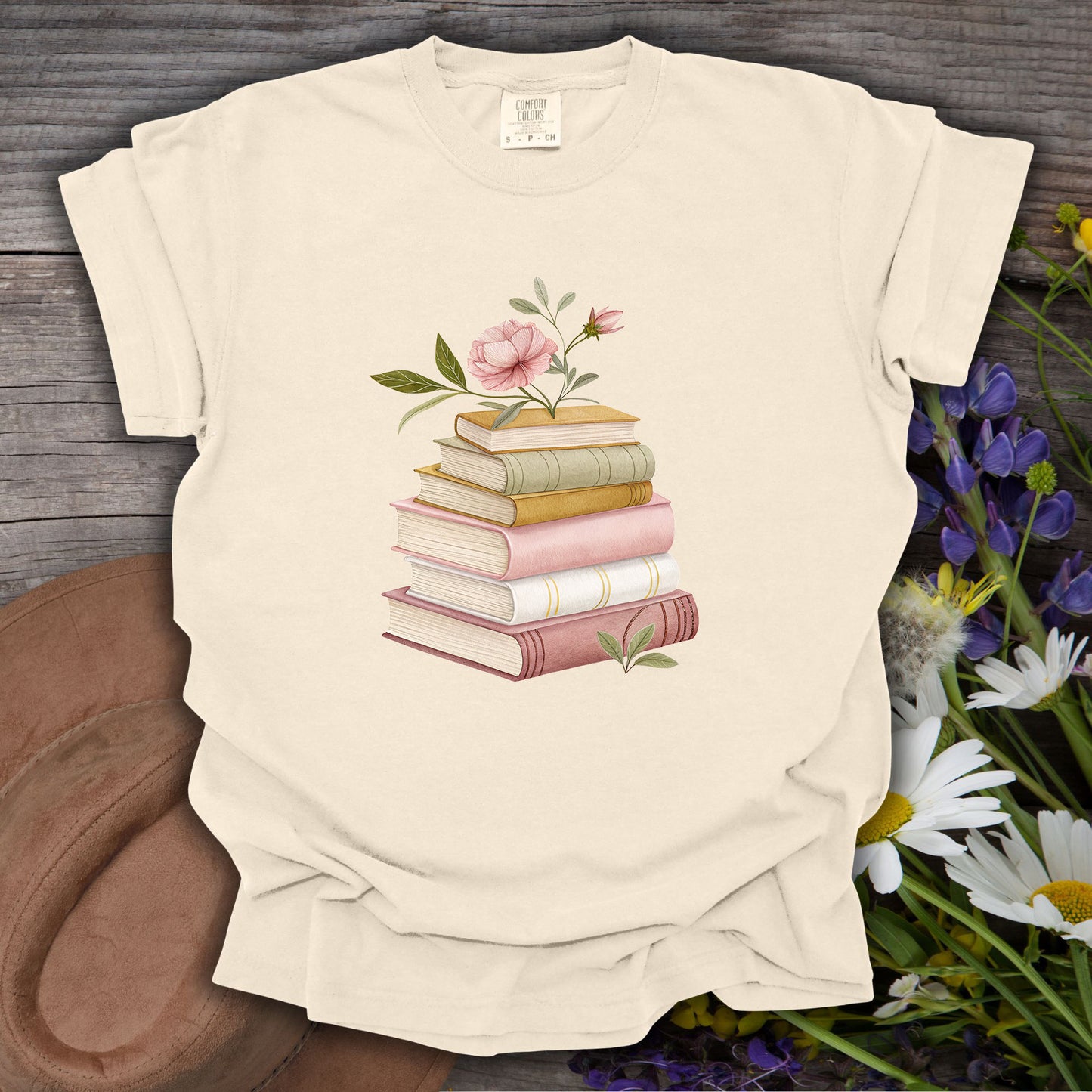 Ivory S Cozy Spring Reading T-Shirt with watercolor books and pink floral design on wood.