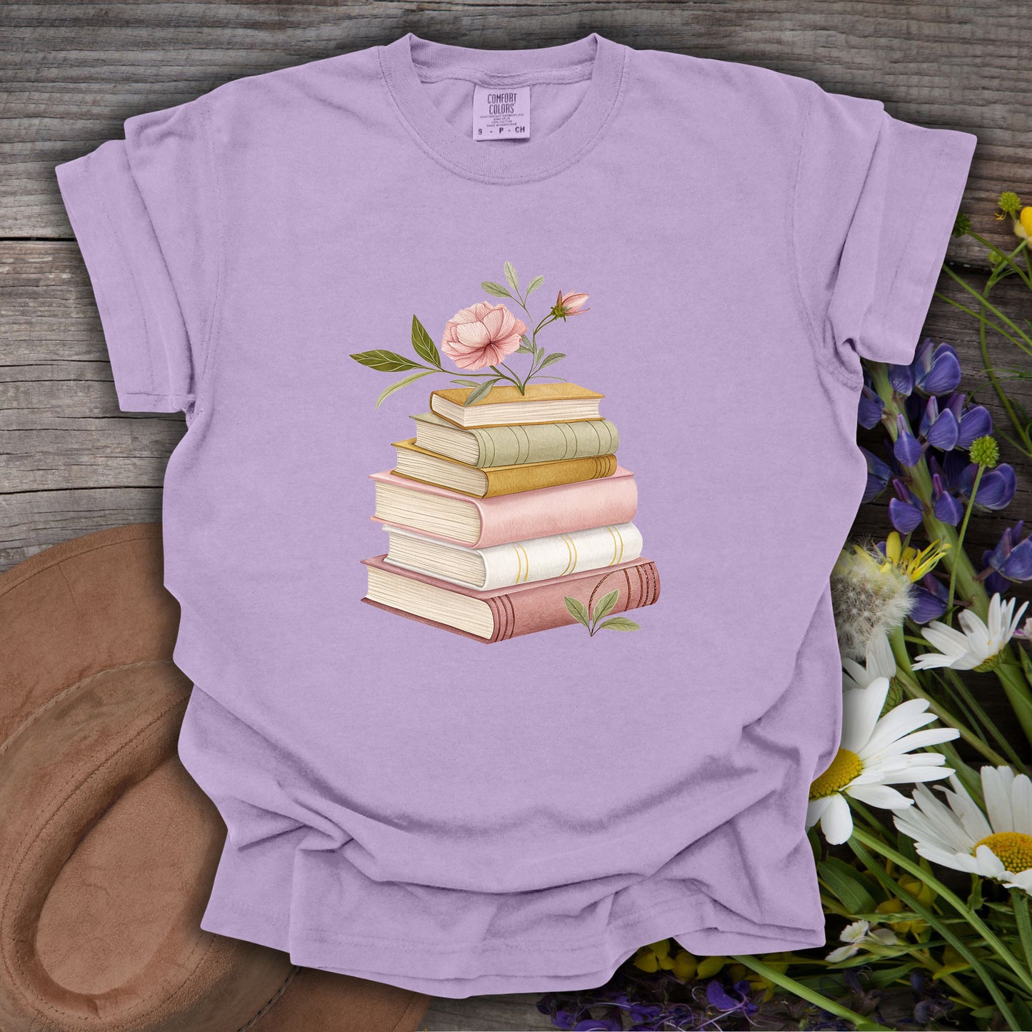 Orchid S t-shirt with a watercolor stack of books and pink floral illustration on wood.
