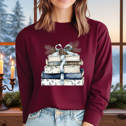 Maroon long sleeve tee with a stack of blue and white books, ribbon, evergreen, and pinecone design.