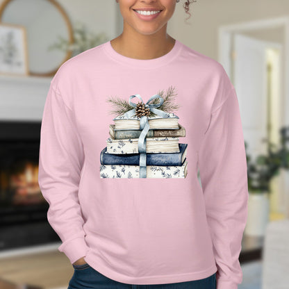 Pink long-sleeve tee with a stack of blue and white books, ribbon, evergreen, and pinecone design.