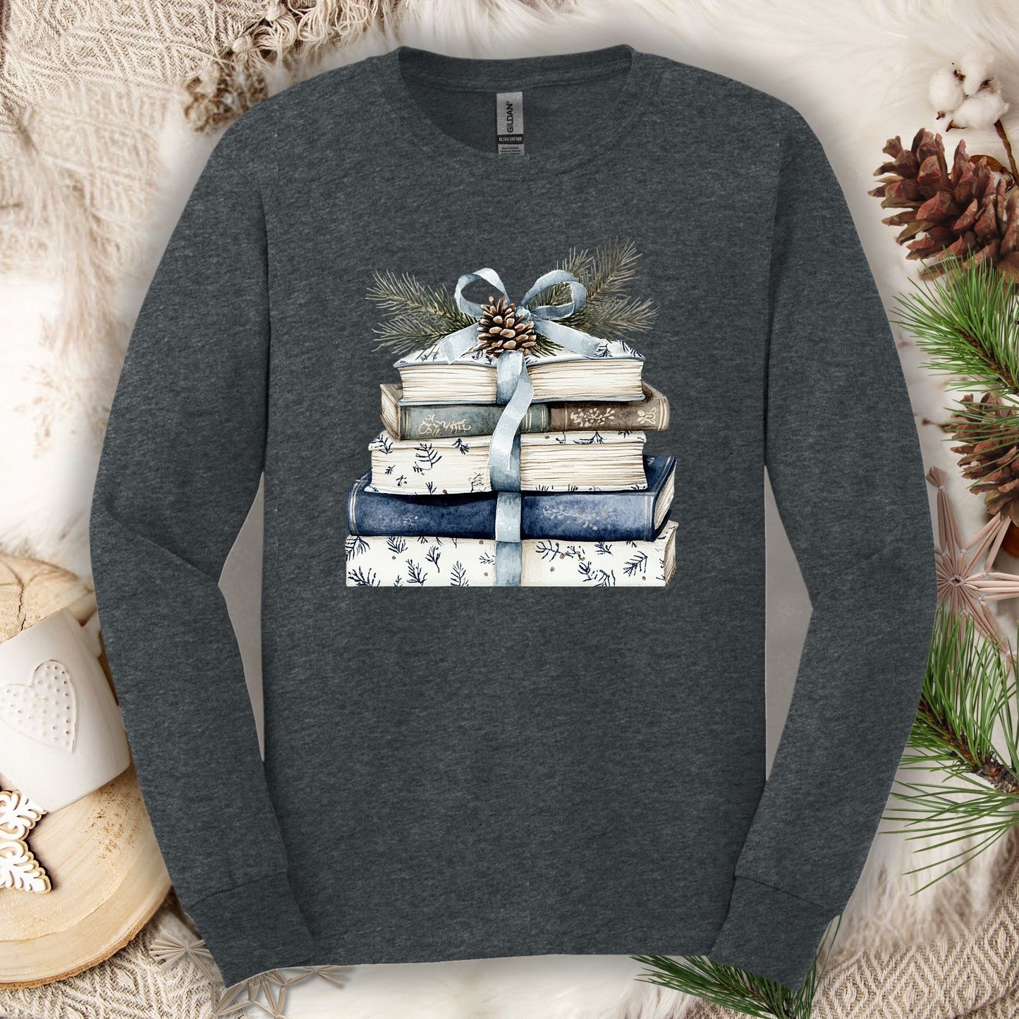 Dark Heather long sleeve tee with a stack of blue and white books, ribbon, evergreen, and pinecone.