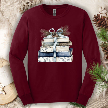 Maroon long-sleeve tee with a stack of blue and white books, blue ribbon, evergreen, and pinecone.