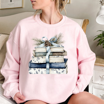 Pink sweatshirt with a stack of blue and white books, blue ribbon, evergreen, and pinecone design.