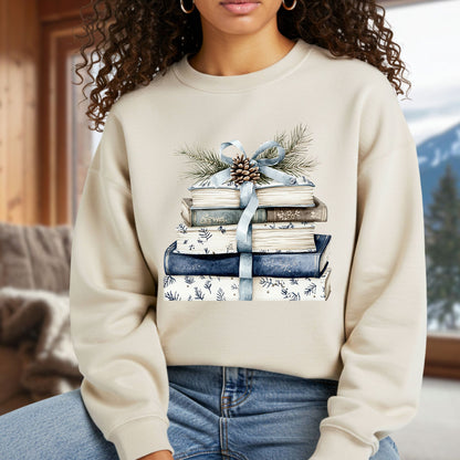 Cozy beige sweatshirt with a stack of blue and white books tied with a blue ribbon, evergreen, and pinecone.