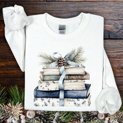 White sweatshirt with a stack of blue and white books, blue ribbon, evergreen, and pinecone design.