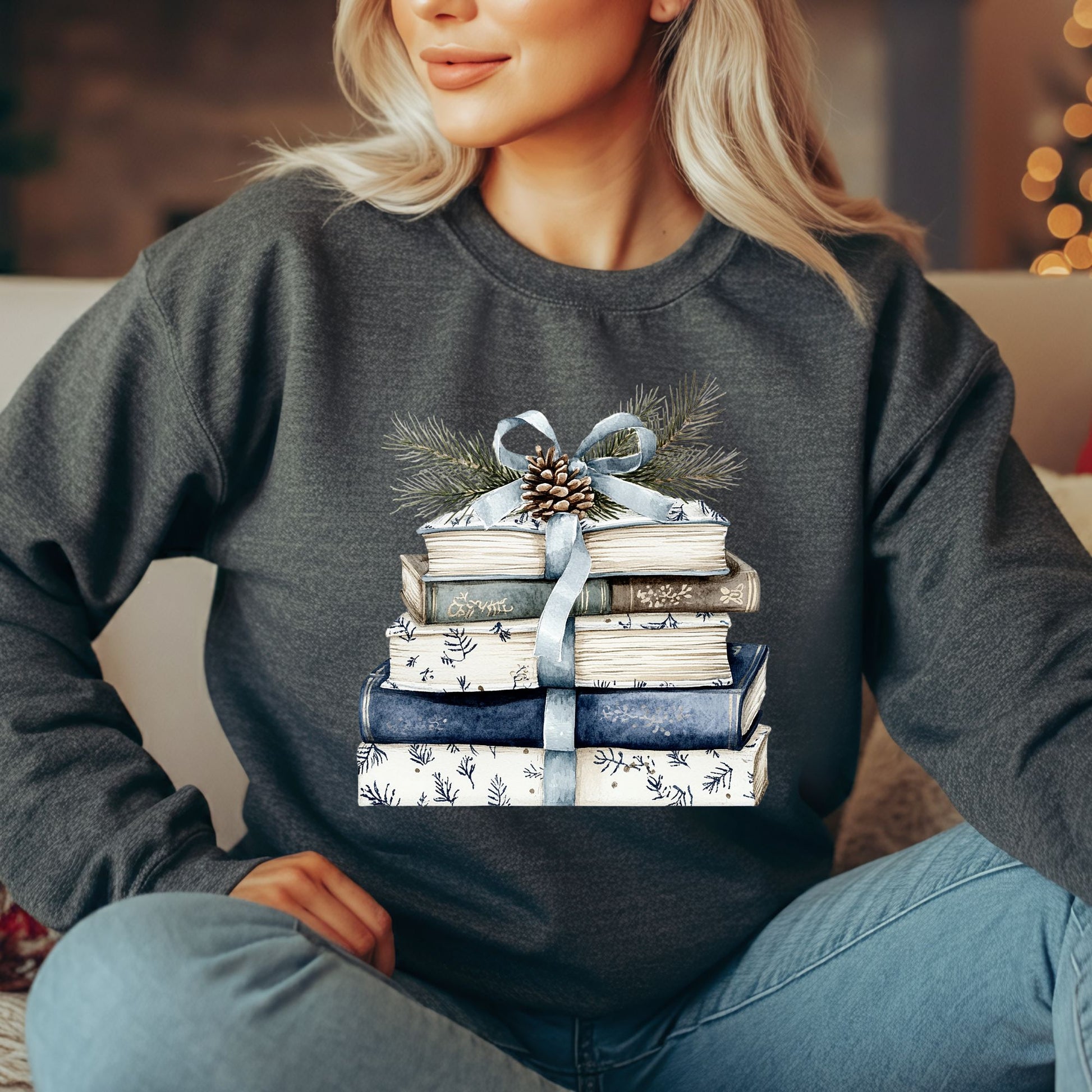 Woman in a charcoal gray sweatshirt with a stack of blue and white books, ribbon, evergreen, and pinecone design.