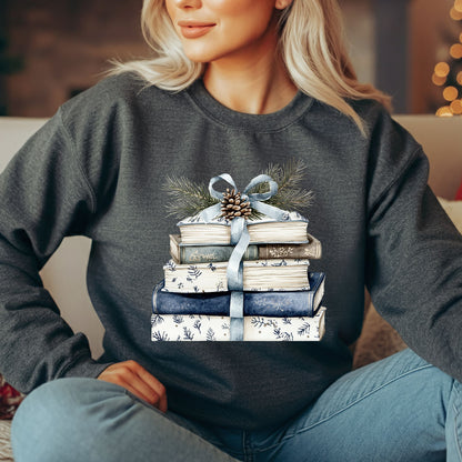 Woman in a charcoal gray sweatshirt with a stack of blue and white books, ribbon, evergreen, and pinecone design.