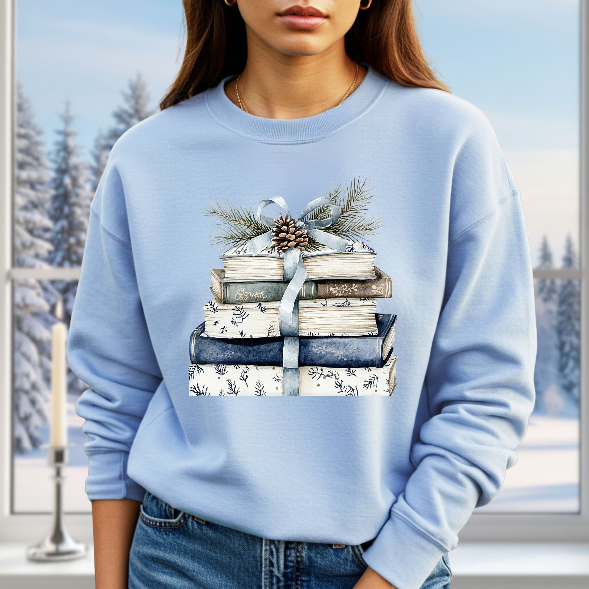 Light blue sweatshirt with a stack of blue and white books, ribbon, pinecone, and evergreen sprig design.