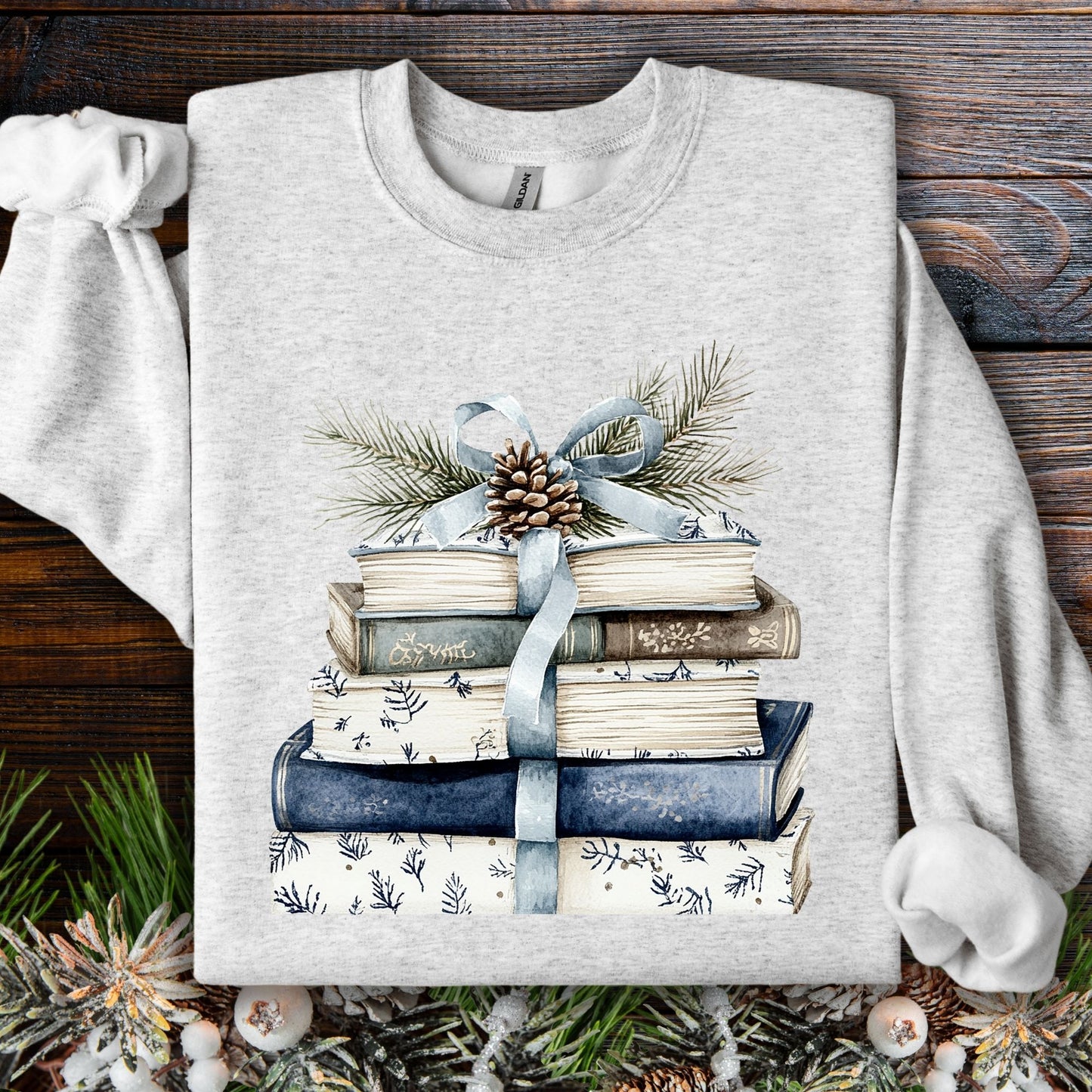 Ash S sweatshirt with blue and white book stack, blue ribbon, evergreen, and pinecone design.